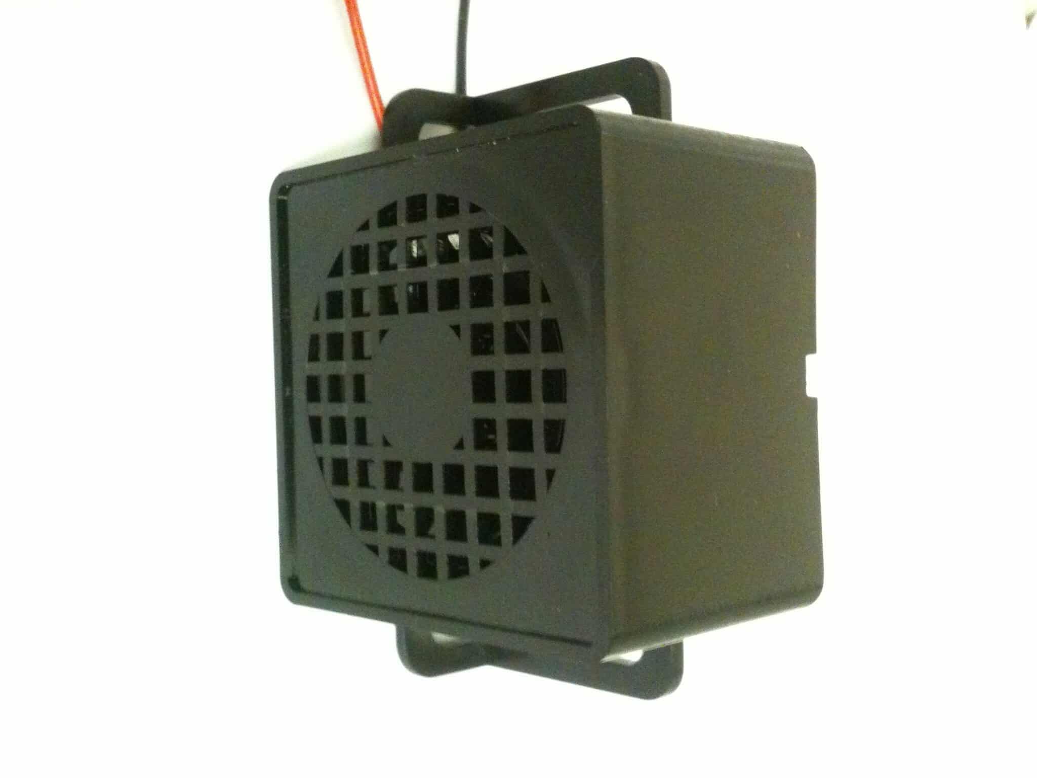 Compact black electronic enclosure with a circular vented grille on the front and a top handle; two wires exit from the top.