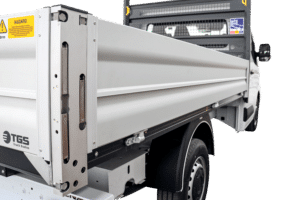 Side view of a white truck with a metal cargo bed; yellow hazard label and the TGS Truck Bodies logo are visible at the rear.
