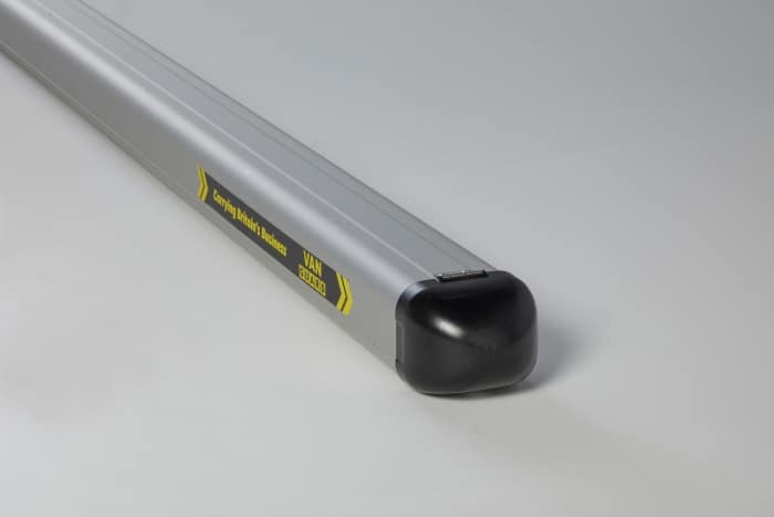 Silver roof rack crossbar with a black end cap, featuring a yellow label, shown on a plain surface (car cargo accessory).