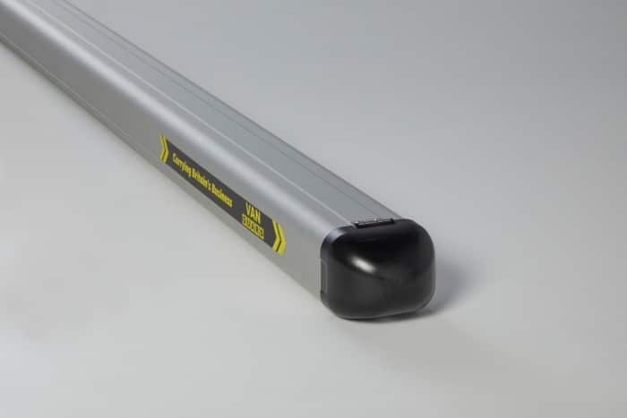 Aluminum roof rack crossbar with black end cap and caution label visible on its side (informational product image).